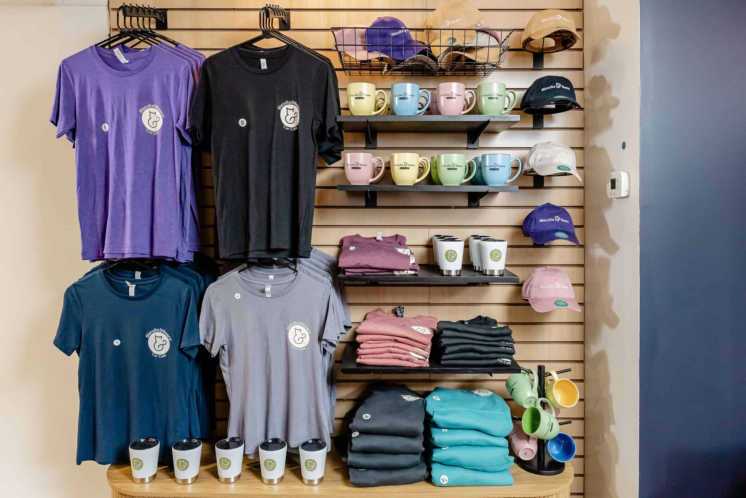 Display of café merchandise including T-shirts, mugs, and caps at Biscuit & Beans Cat Café.